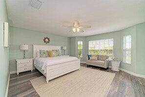 A bedroom with a bed, nightstands, a dresser, a ceiling fan, and a window with blinds. - Kickback Cabana managed by Beach Retreats (Holmes Beach)
