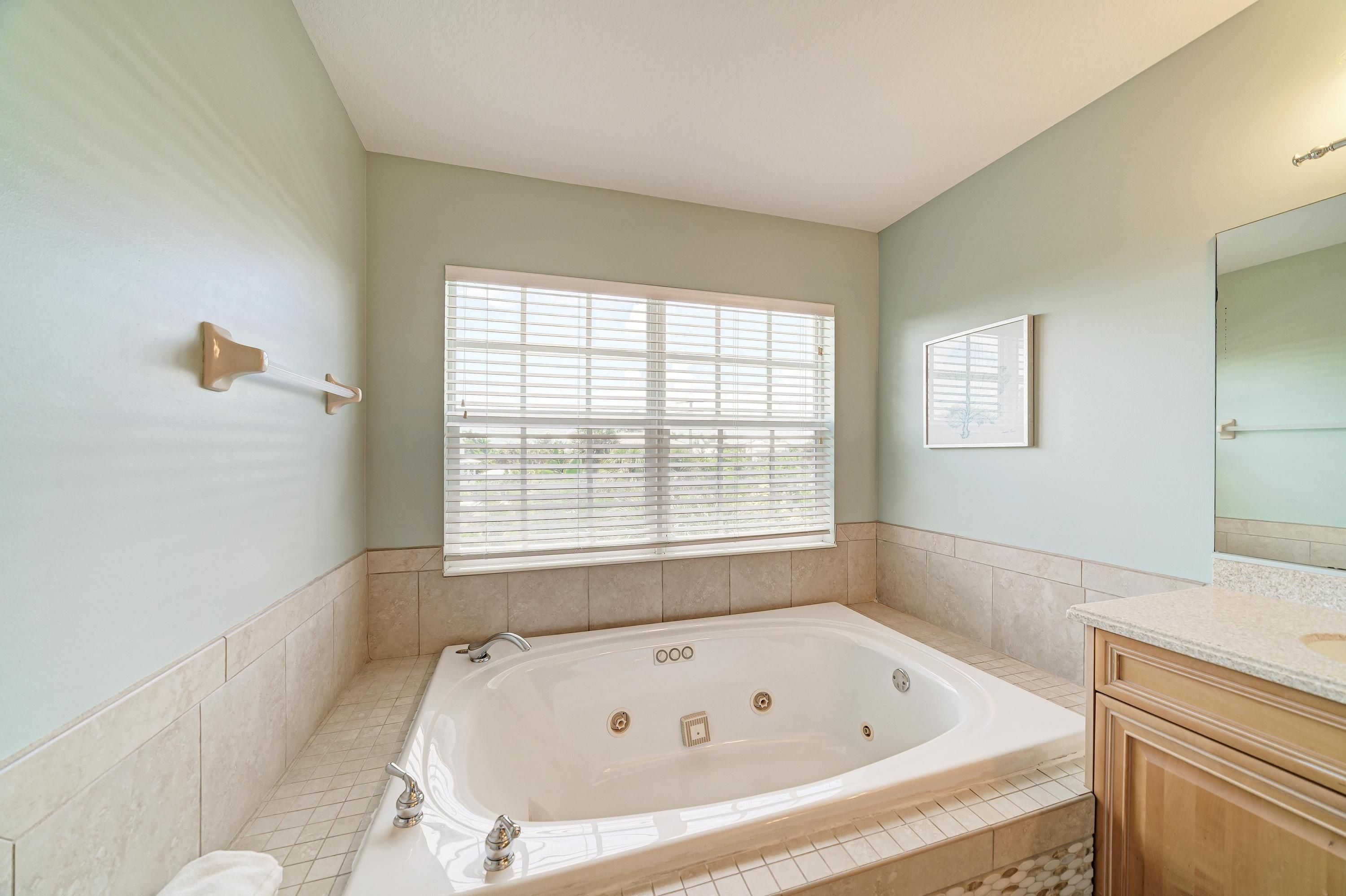 A bathroom with a freestanding bathtub, a large window with blinds, and a mirror on the wall.