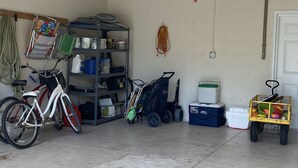 A garage with a bicycle, shelves with various items, a cooler, and a cart with colorful objects. - Kickback Cabana managed by Beach Retreats (Holmes Beach)