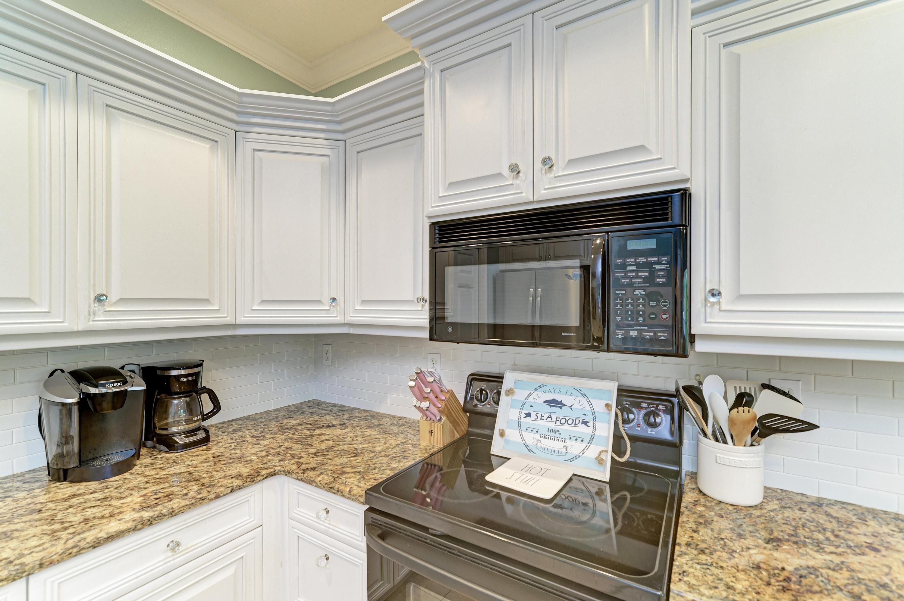 A kitchen with white cabinetry, a built-in microwave, a Keurig coffee maker, and a sign on the oven.