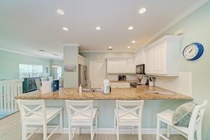 A kitchen with a granite countertop, white cabinetry, and a clock on the wall.
