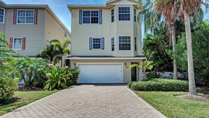 A two-story residential building with a garage, surrounded by a paved driveway and lush landscaping. - Kickback Cabana managed by Beach Retreats (Holmes Beach)