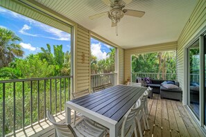A covered outdoor area with a table and chairs, a ceiling fan, and a view of lush greenery. - Kickback Cabana managed by Beach Retreats (Holmes Beach)