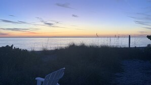 A beach scene with a chair and a fence in the foreground. - Kickback Cabana managed by Beach Retreats (Holmes Beach)