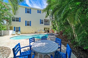 A two-story building with a swimming pool, outdoor seating, and lush greenery.