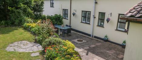 Une maison avec un toit en tuiles, un jardin agrémenté de pas japonais et une terrasse avec une table et des chaises.