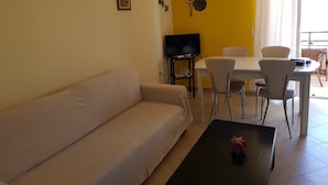Olohuoneessa on sohva, sohvapöytä, televisio sekä ruokailutila, jossa on tuoleja ja pöytä.