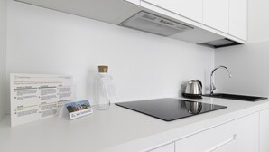 A modern kitchen with white cabinetry, a stainless steel kettle, and a black induction cooktop. A recycling sign is visible on the wall. - Italianway - Mauro Macchi 65 (Milan)