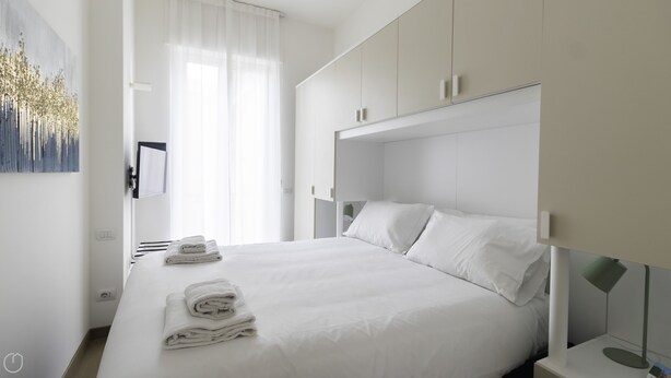 A modern bedroom with a large bed, white bedding, and a neatly folded towel on the side. - Italianway - Mauro Macchi 65 (Milan)