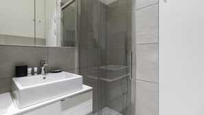 Features a sleek sink, large mirror, and glass-enclosed shower area.