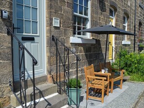 A stone building with a white door, a black metal staircase, and a wooden table with chairs and a black umbrella. - No. 4 Embsay (Skipton)