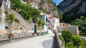 A narrow street with buildings on a hillside, stone walls, and potted plants. - Medusa Suite in Positano (Positano)