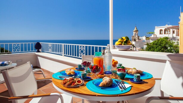A round wooden table set with breakfast items, a view of the sea, and a balcony railing. - Medusa Suite in Positano (Positano)