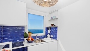 A modern kitchen with a view of the sea, white cabinets, a sink, and a blue backsplash. - Medusa Suite in Positano (Positano)