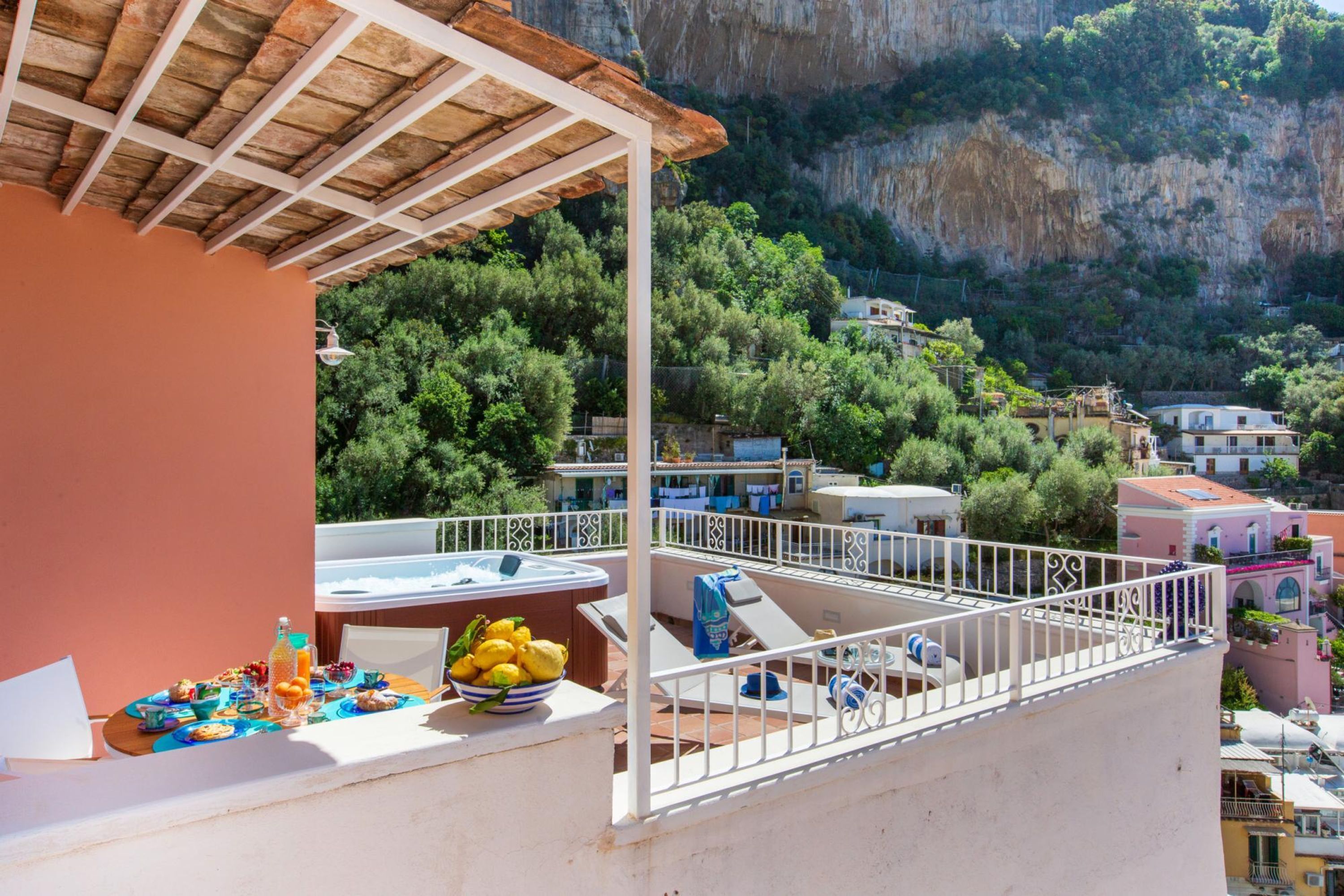 A balcony with a table set for breakfast, overlooking a mountainous landscape with buildings.