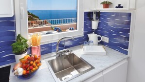 A kitchen with a stainless steel sink, a bowl of fresh produce, a potted plant, and a view of the sea through a window. - Medusa Suite in Positano (Positano)