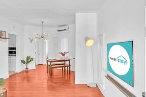 Ein modernes Hotelzimmer mit Holzboden, einer Essecke mit Tisch und Stühlen, einer Kristallleuchter und einem an der Wand befestigten Schild.