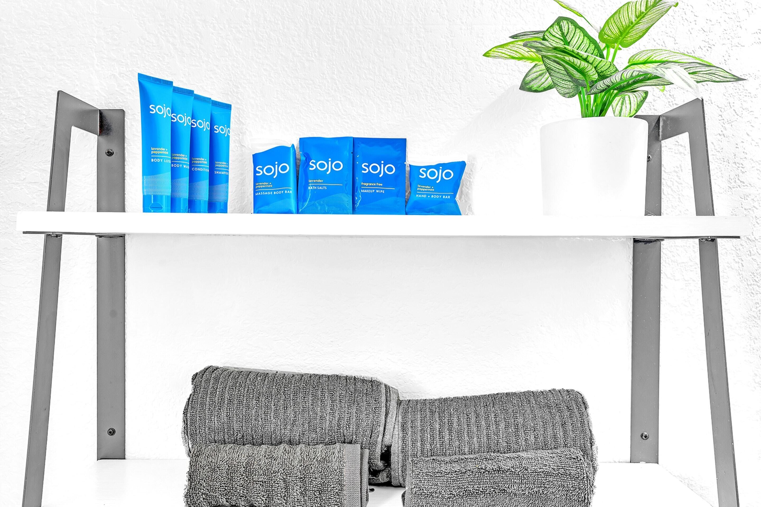 A white shelf with blue body care products, a potted plant, and grey towels.