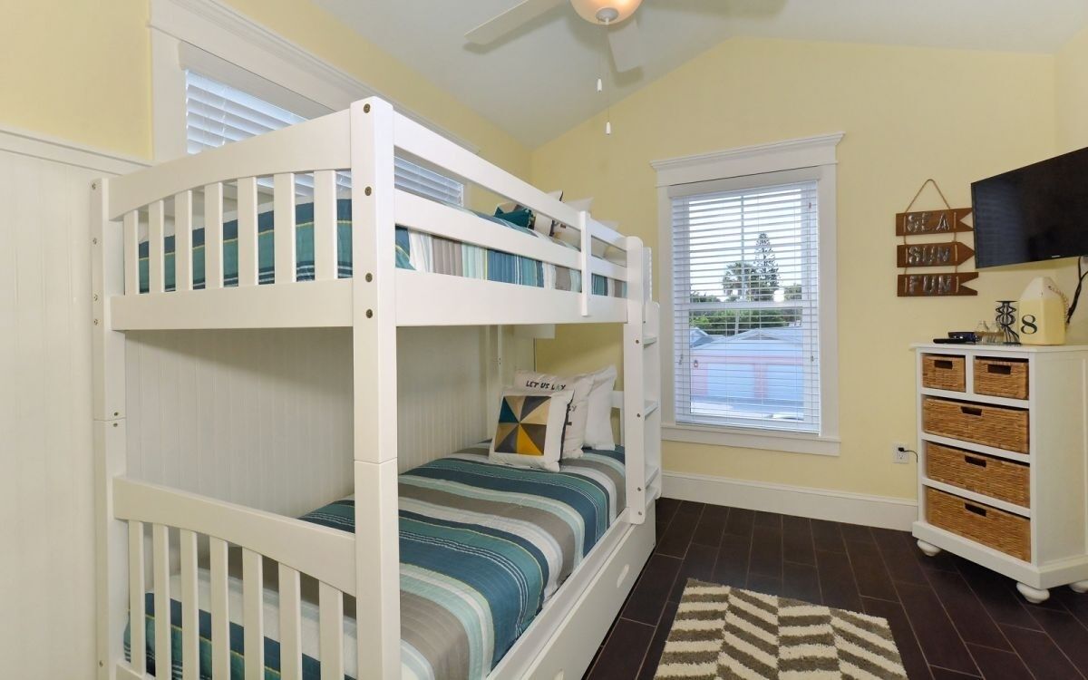 A room with bunk beds, a television, a window with blinds, and a dresser with baskets.