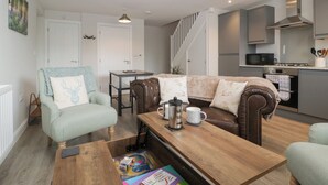 A cozy living room with a sofa, a coffee table, and a dining table. There is a kitchen area with a microwave and stove. - The Old School (Ross-on-Wye)