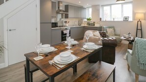 A modern kitchen with grey cabinets, a dining area with a wooden table set for four, and a cozy living space with a sofa and a lamp. - The Old School (Ross-on-Wye)
