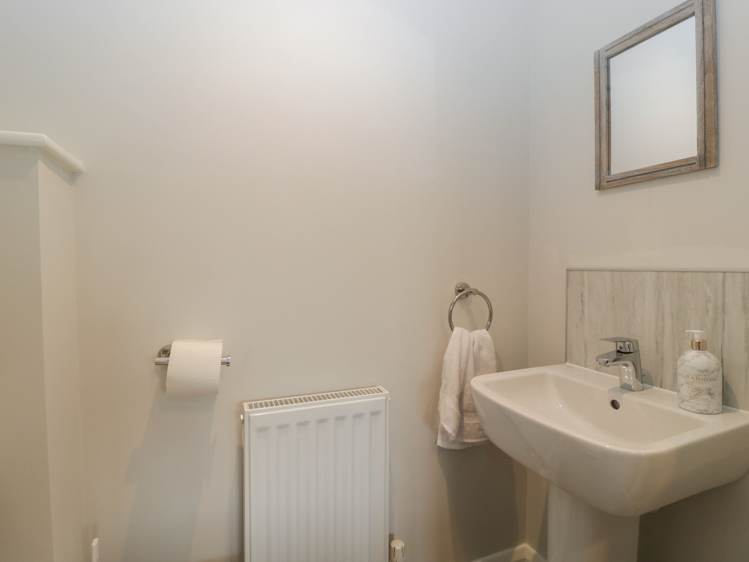 A bathroom with a white sink, a mirror, a towel ring, and a toilet paper holder.