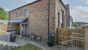 A stone building with a patio area, outdoor seating, and a wooden gate. - The Old School (Ross-on-Wye)