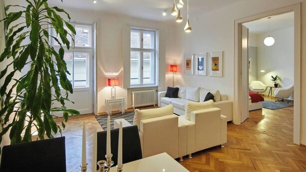 A modern living room with a white sofa set, a dining table with candles, and a large green plant.