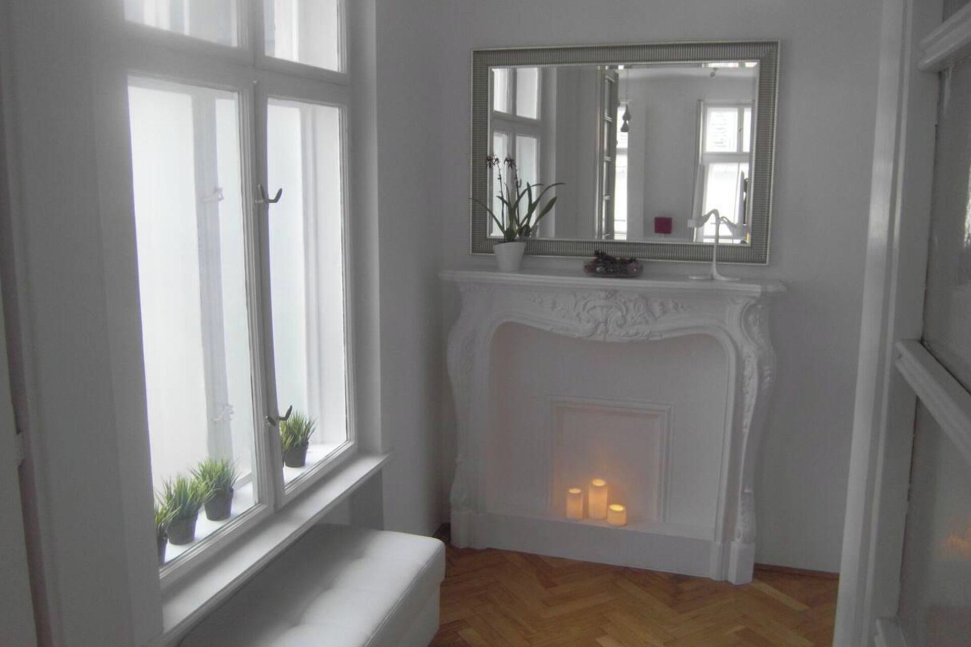 Una habitación con chimenea blanca, un banco y una ventana con plantas.