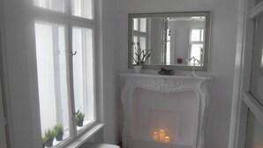 A room with a white fireplace, a bench, and a window with plants.
