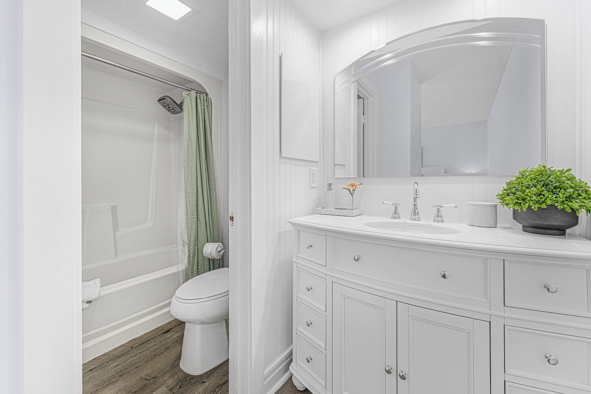 Une salle de bain avec une douche, des toilettes, un meuble-lavabo avec des tiroirs, un miroir et une plante en pot.