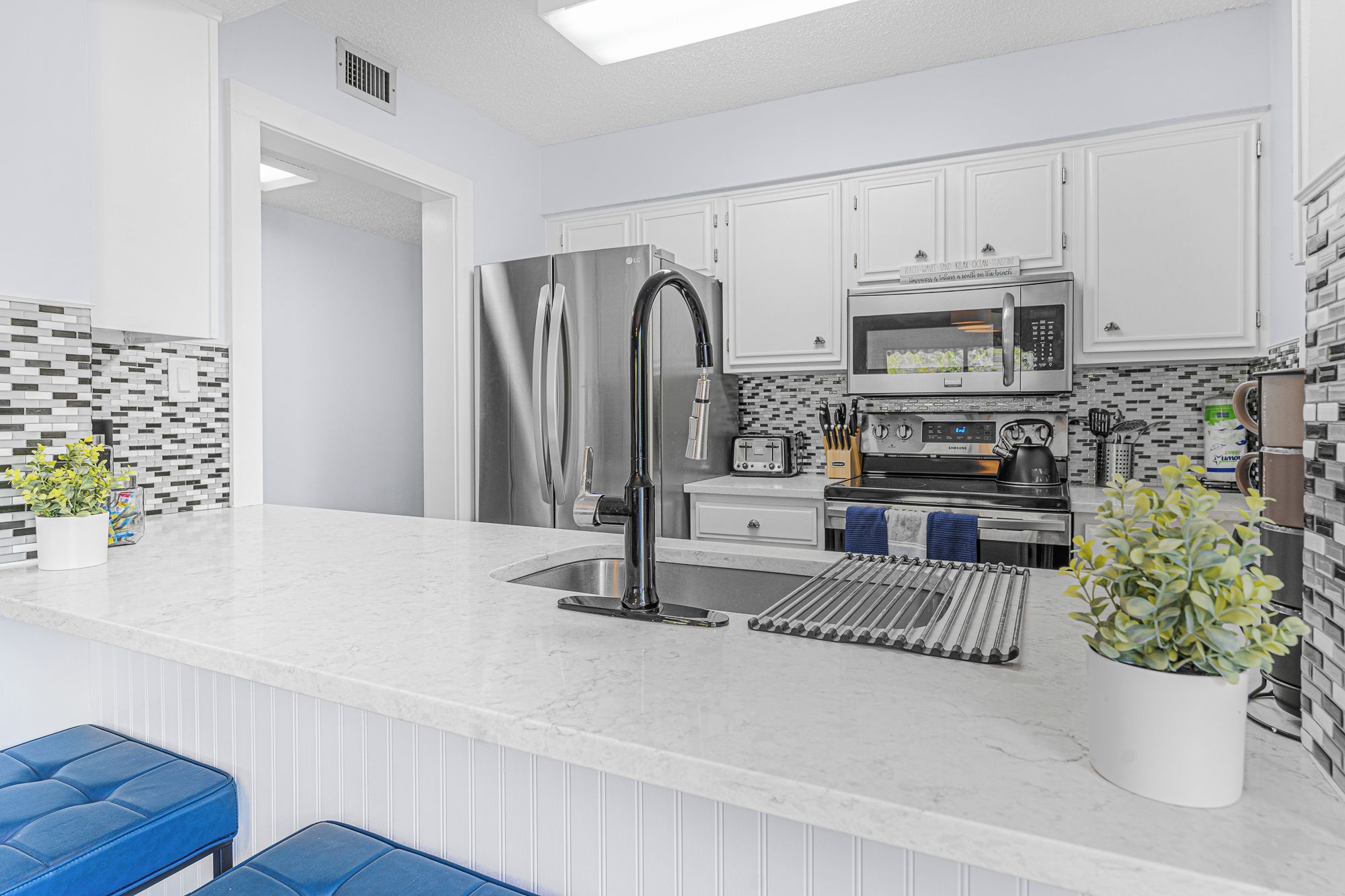 A modern kitchen with white cabinetry, stainless steel appliances, and a marble countertop.