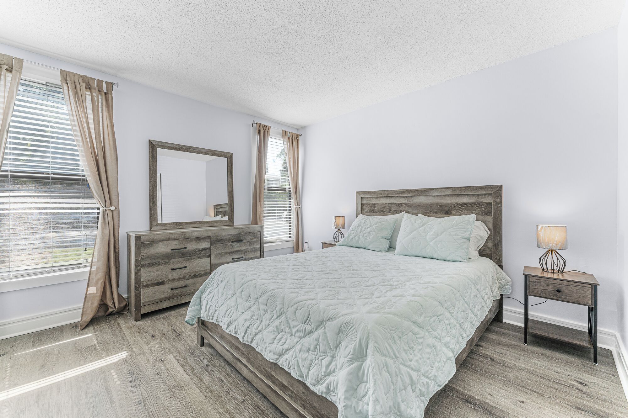 A bedroom with a bed, a dresser, a nightstand, a lamp, and a mirror.