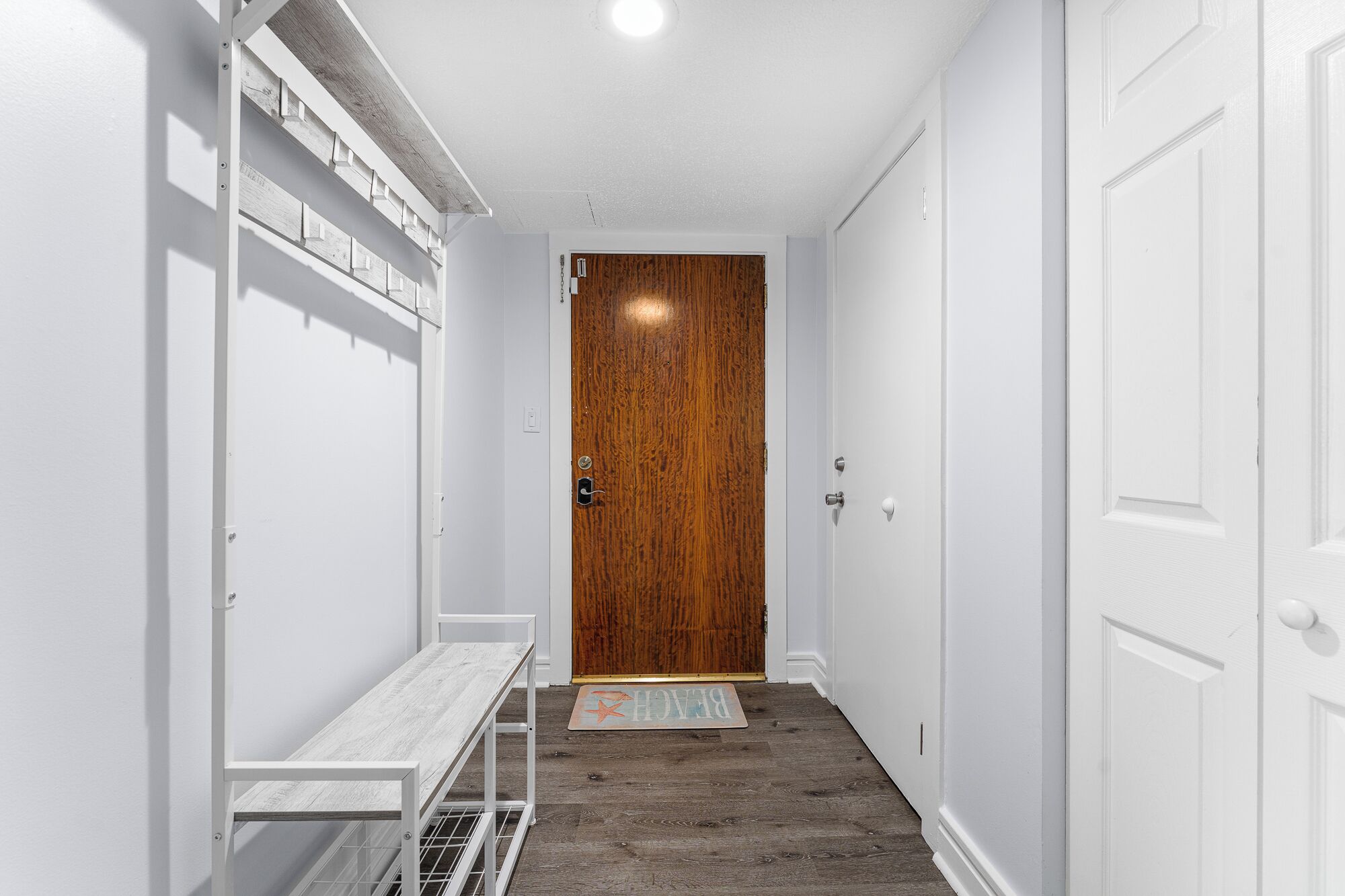 Un pasillo estrecho con una puerta de madera al final, un banco blanco y un felpudo con diseño de estrella en el suelo.