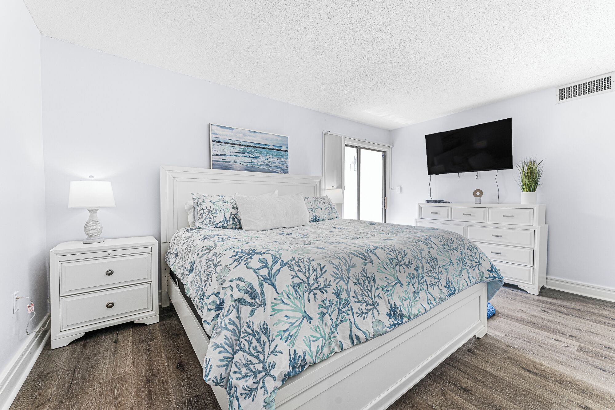 A bedroom with a bed, nightstands, a dresser, a TV, and a painting on the wall.