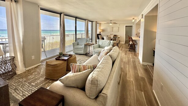 Ein großzügiger Wohnbereich mit einer großen Couch, einem Couchtisch und einem Essbereich mit Stühlen. Große Fenster bieten Blick auf den Strand.