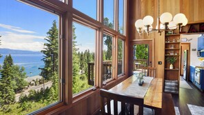 A wooden interior with large windows overlooking a forest and a body of water. - Eagles Perch Cabin - Pano Lake Views, Fido Friendly (Carnelian Bay)