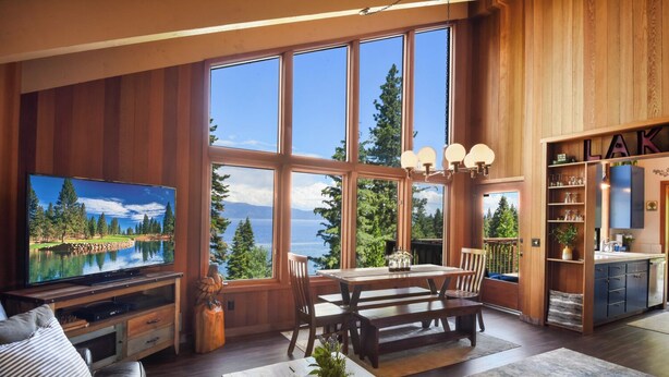 A spacious living room with a large TV, wooden furniture, and a view of the lake. - Eagles Perch Cabin - Pano Lake Views, Fido Friendly (Carnelian Bay)