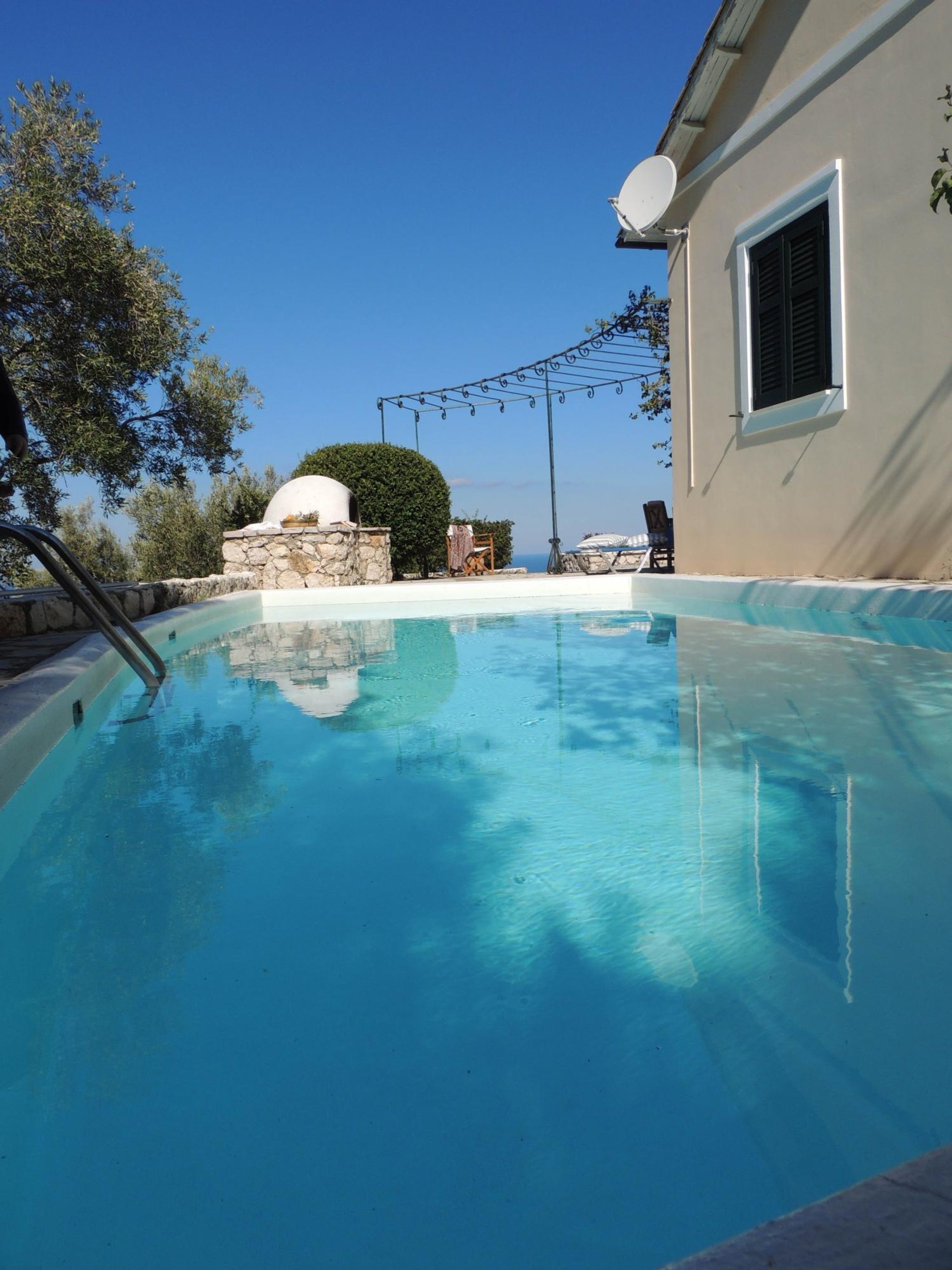 Une piscine dotée d’une structure en pierre et, en arrière-plan, un bâtiment blanc.