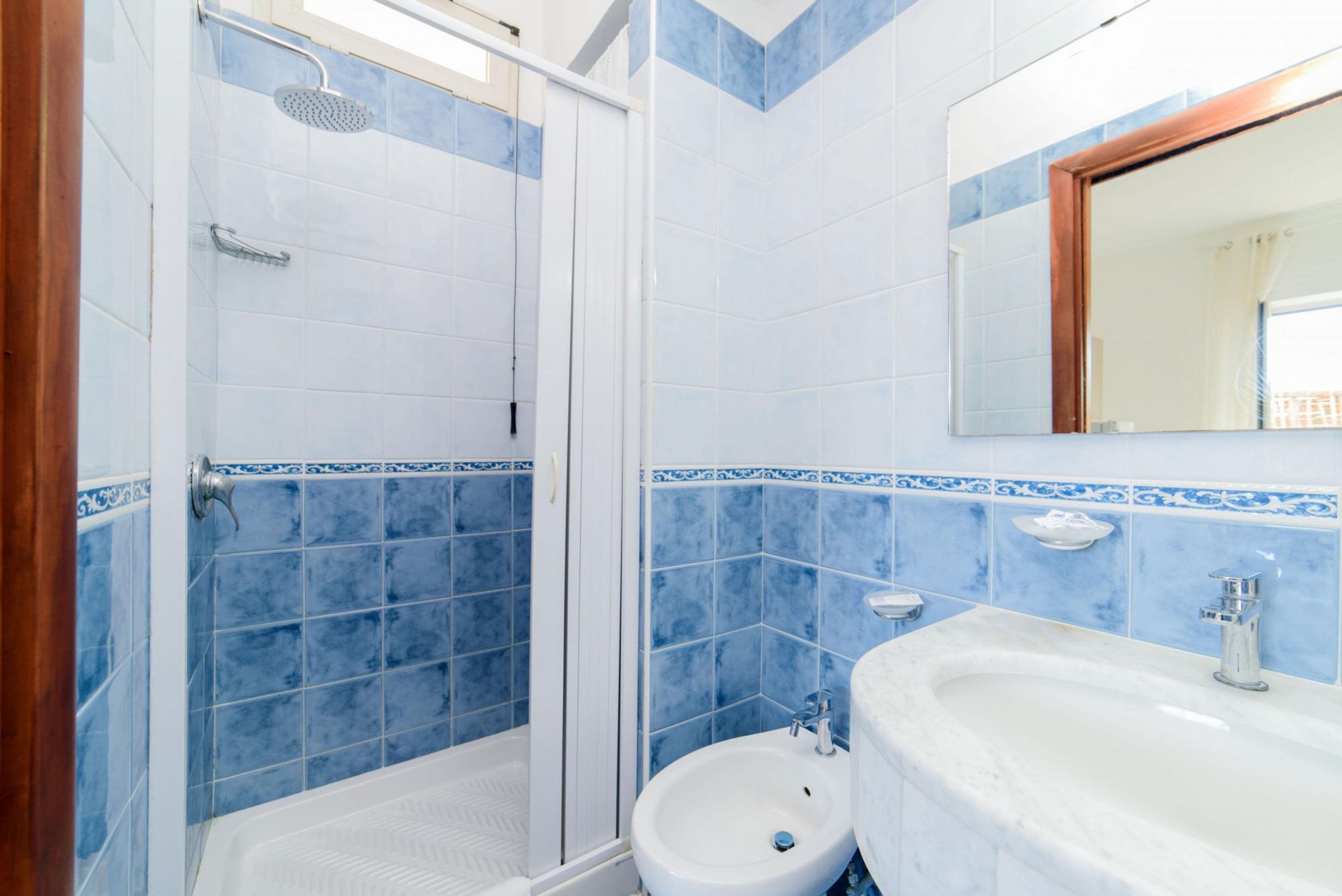 Ein Badezimmer mit Dusche, Toilette und Waschbecken, wobei alle Wände blau gefliest sind.