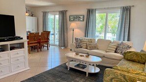 A living room with a sofa, coffee table, TV, and a dining area with chairs and a table. - The Sand Castle (St. Augustine)