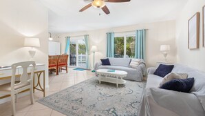 A spacious living room with a ceiling fan, a sofa, a coffee table, and a dining area with chairs and a table. - The Sand Castle (St. Augustine)