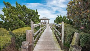 A wooden boardwalk leading to a gazebo in a landscaped area with trees and shrubs. - The Sand Castle (St. Augustine)