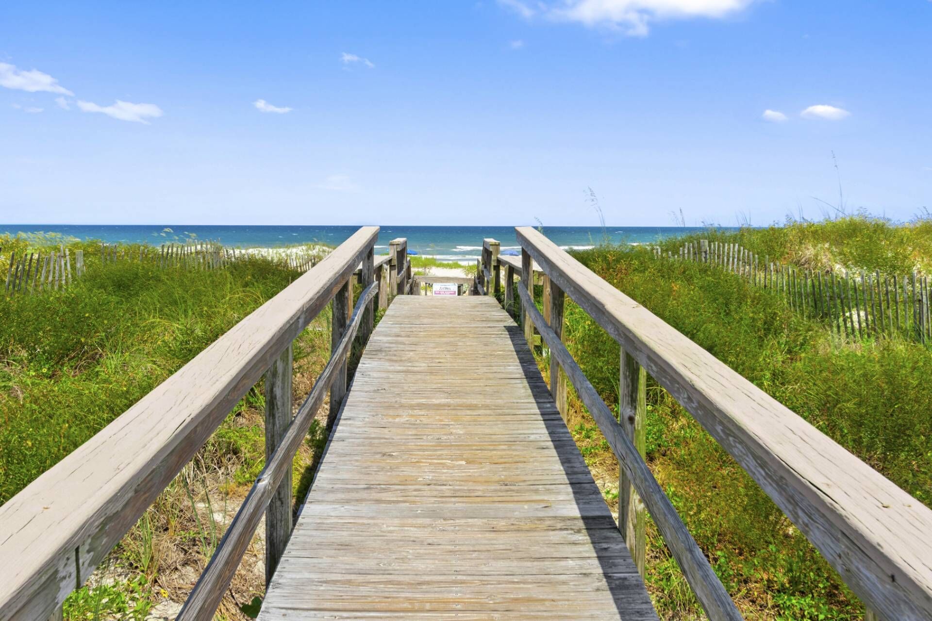 A wooden boardwalk leading to a beach with a clear sky.