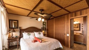 A bedroom with a wooden ceiling, a bed with a white bedspread, a nightstand with a lamp, and a wooden wardrobe.
