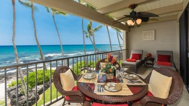 A dining area with a view of the ocean, featuring wicker furniture and a table set for two.