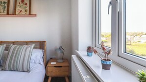Ein Schlafzimmer mit Bett, Nachttisch, Lampe und Fenster mit Blumentöpfen.