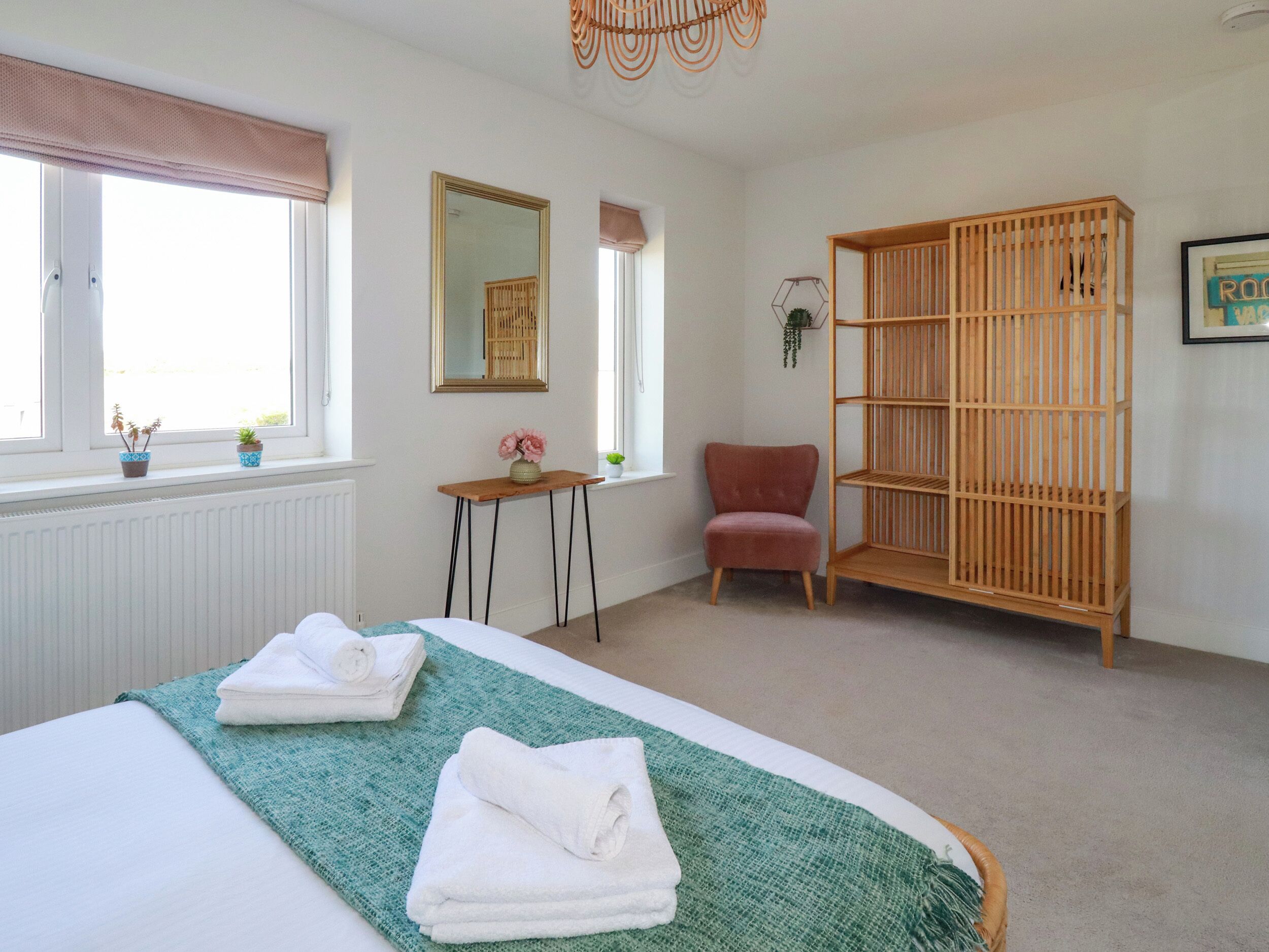 A hotel room with a bed, a wooden chair, a small table, a mirror, and a wooden bookshelf.