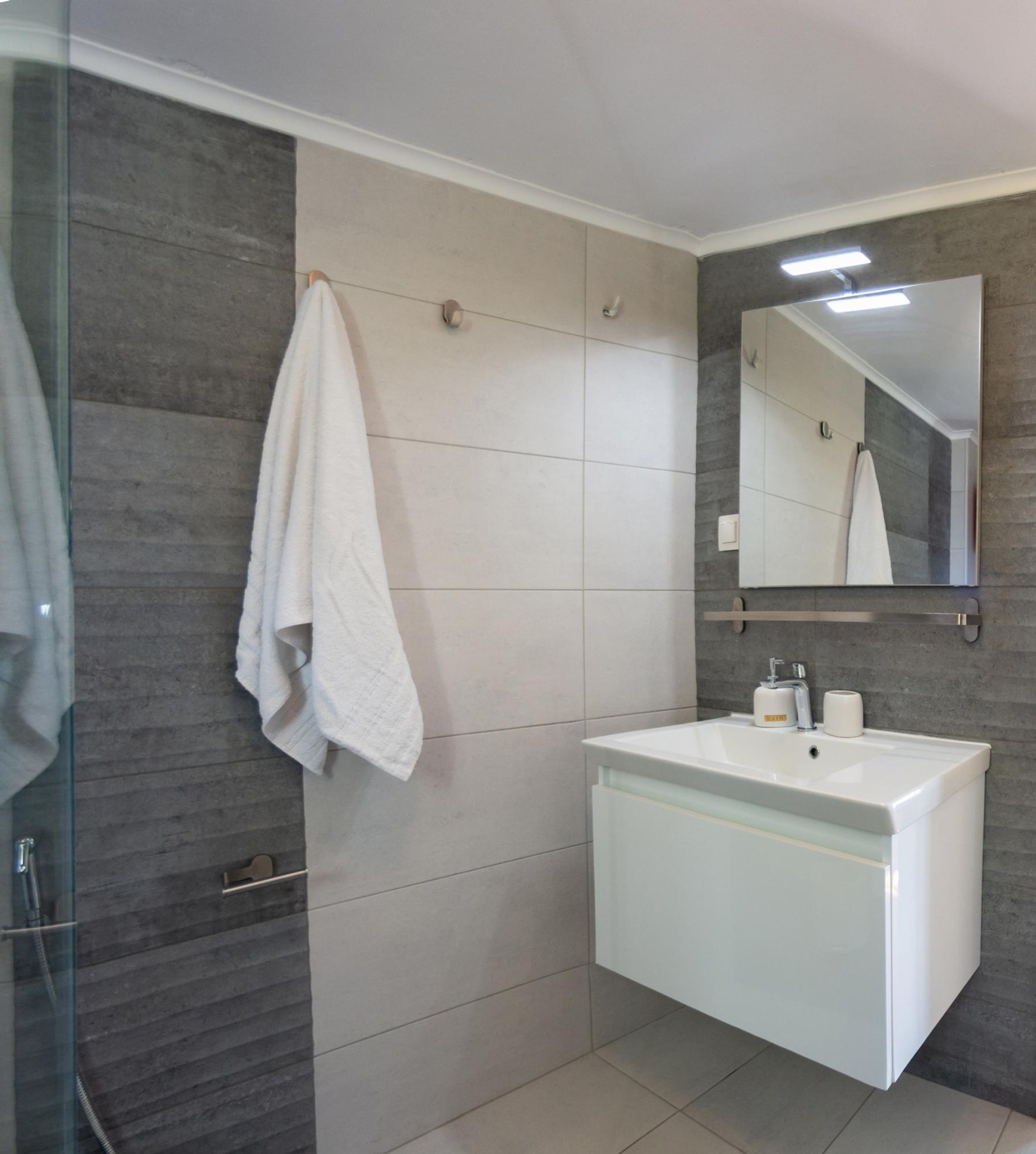 A bathroom with a white sink, a mirror, and a towel hanging on the wall.