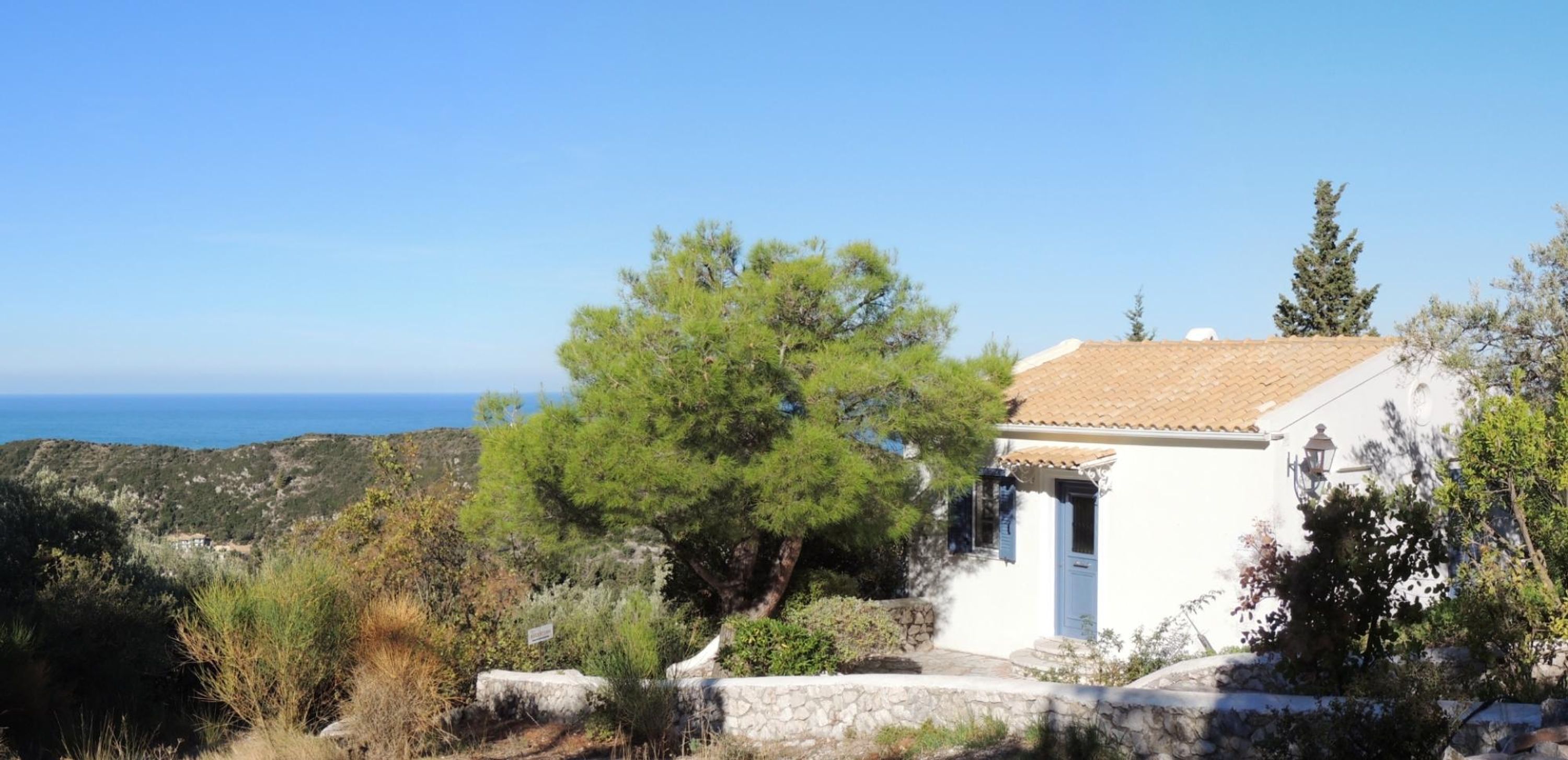 Un edificio blanco con tejado de baldosas, pared de piedra y vista al mar.
